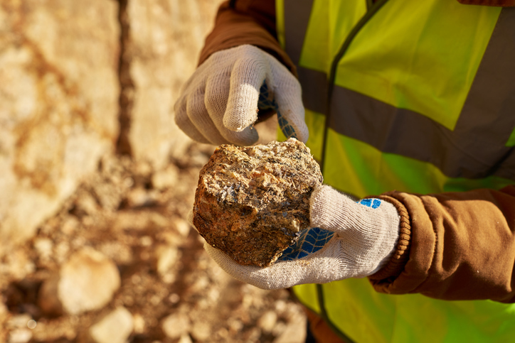 Close up of industrial worker holding mineral ore in gloved hands on mining site, copy space